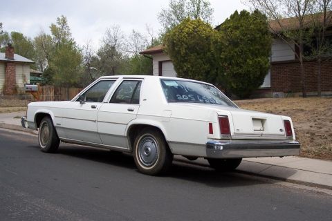1972 Ford Ranchero - White sedan parked on street with numbers written on the rear window.