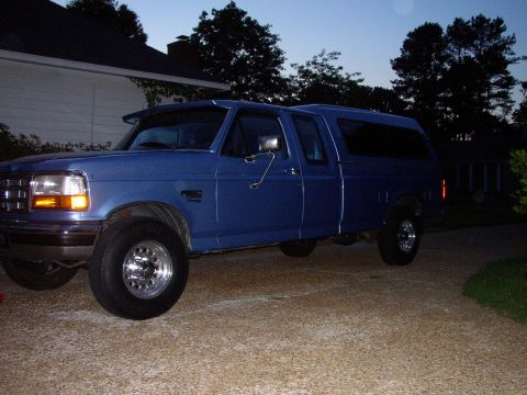 1995 Ford Bronco - Blue Ford pickup truck with a camper shell parked in a driveway at dusk.