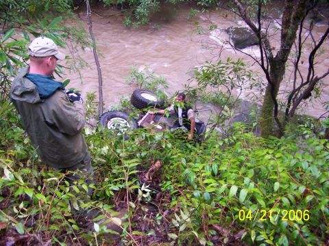 1995 Ford Bronco - Two people stand near an off-road vehicle that has gone into a creek.