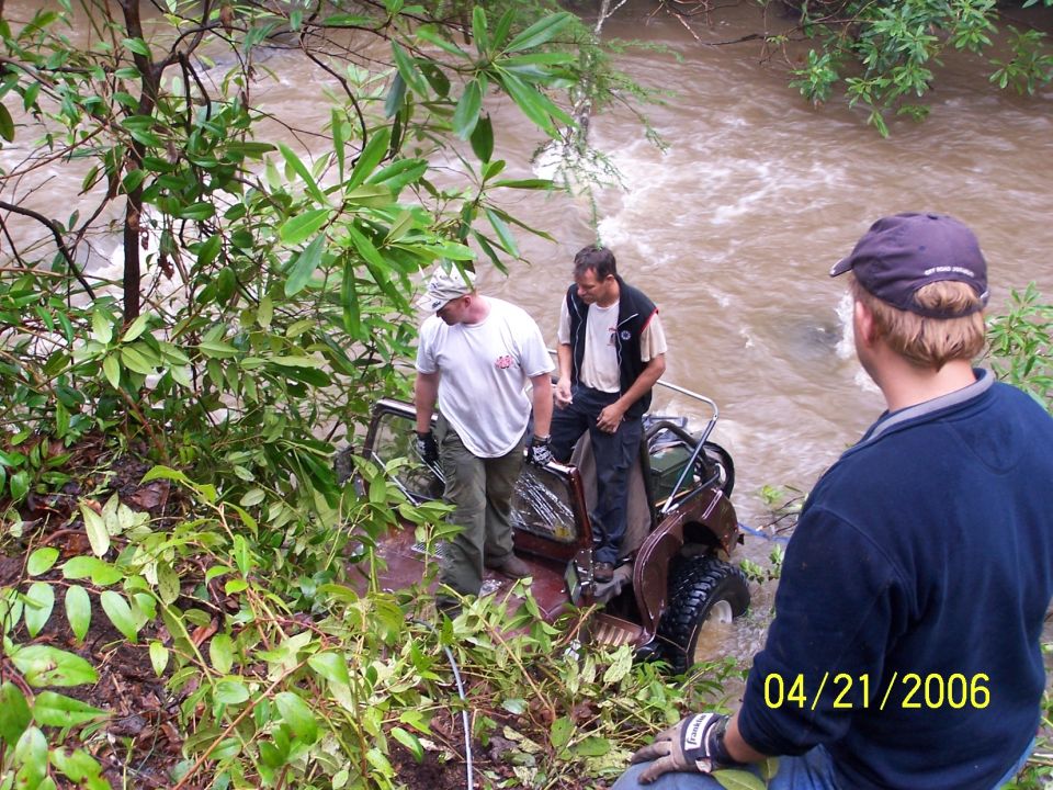 Men recovering a dark red Jeep rolled on its side in a muddy river, 2006