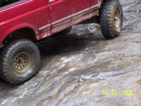1995 Ford Bronco - A red SUV navigates a challenging rocky path, its large tires gripping the uneven surface.