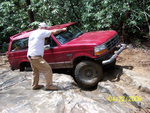 1995 Ford Bronco - A red Ford Bronco navigates a difficult rocky terrain, with its roof appearing to be compromised.