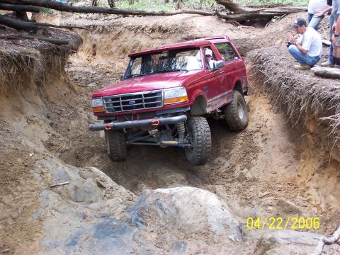 1995 Ford Bronco - A red 1995 Ford Bronco is shown off-roading on a challenging, muddy trail.