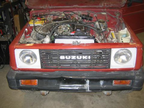 1987 Suzuki Samurai - Front view of a red 1987 Suzuki Samurai with its hood open, revealing the engine compartment and the prominent SUZUKI grille badge.