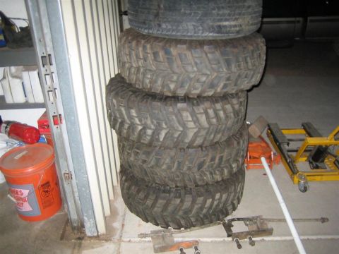 1987 Suzuki Samurai - A stack of four off-road tires sits in a garage next to a red bucket and some tools.