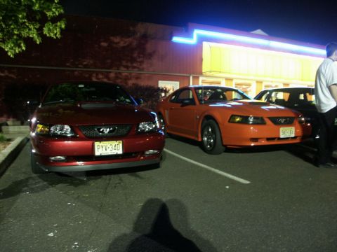 2001 Mercury Grand Marquis - Two Ford Mustangs, one red and one orange, are parked in a lot at night. The red Mustang is in the foreground.