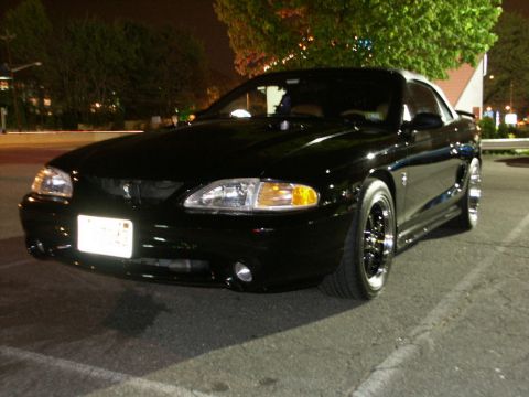 2001 Mercury Grand Marquis - A black Ford Mustang is parked in a lot at night, showing its front quarter profile and custom wheels.