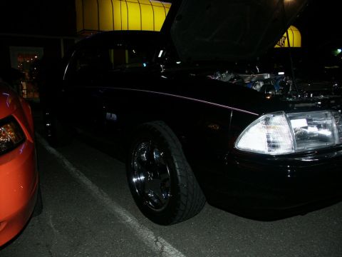 2001 Mercury Grand Marquis - A dark sedan with its hood up is parked next to an orange vehicle at night.