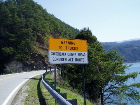2002 Harley-Davidson Sportster Custom - Roadside warning sign for trucks about switchback curves ahead, set against a scenic mountain and water backdrop.
