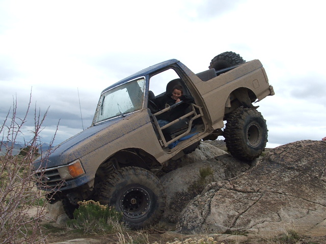 Modified 1987 Ford Bronco with large tires climbing over large rocks off-road
