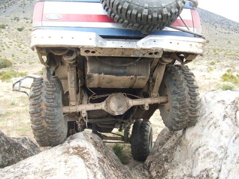1989 Ford Bronco - This modified truck is shown from the rear, with its undercarriage and suspension clearly visible as it drives over rocks.