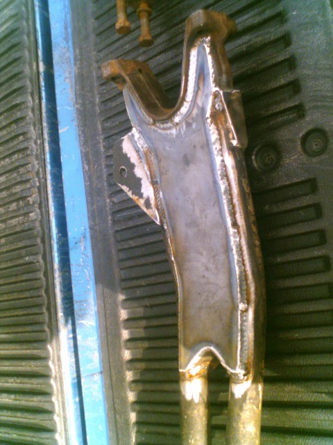 1989 Ford Bronco - A close-up of a welded metal component, possibly a suspension part, resting on a ribbed surface.