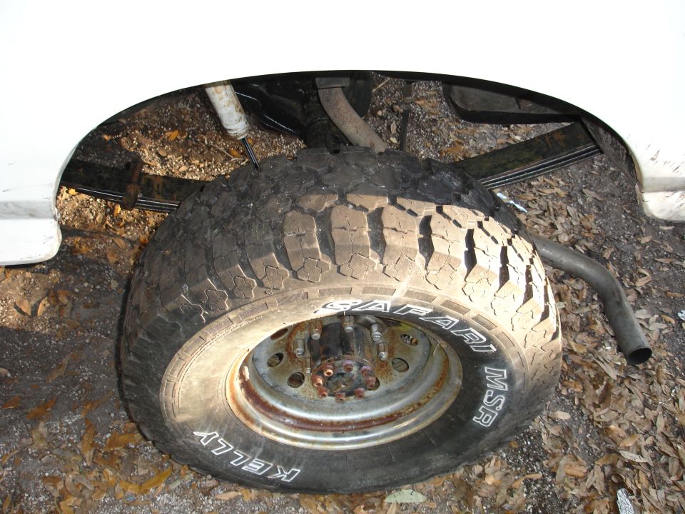 Close-up of a vehicle's rear tire and leaf spring suspension system. The tire is a Kelly Safari MSR