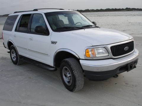1989 Ford Bronco - This white Ford Expedition SUV is seen from a 3/4 front angle on a sandy beach, with the ocean in the background.