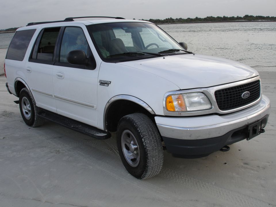 White Ford Expedition SUV parked on a sandy beach, 3/4 front view. Chrome trim and running boards visible