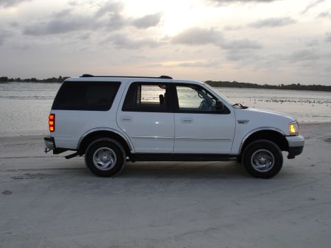 1989 Ford Bronco - This white Ford Expedition is parked on a sandy beach with the ocean in the background.