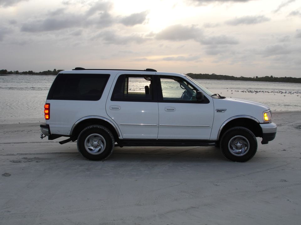 White Ford Expedition parked on a sandy beach near the water