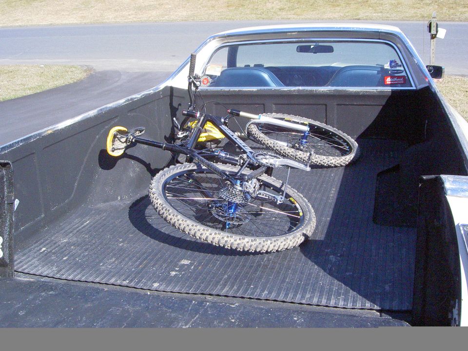 Mountain bike lying in the gray bed of a car-based pickup with rear cab window visible