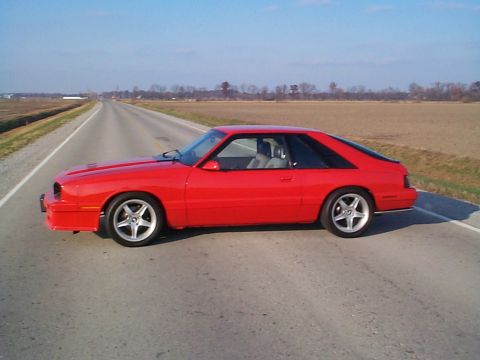 1994 Ford Probe - A red coupe with a distinctive fastback design is parked on the shoulder of an empty road.