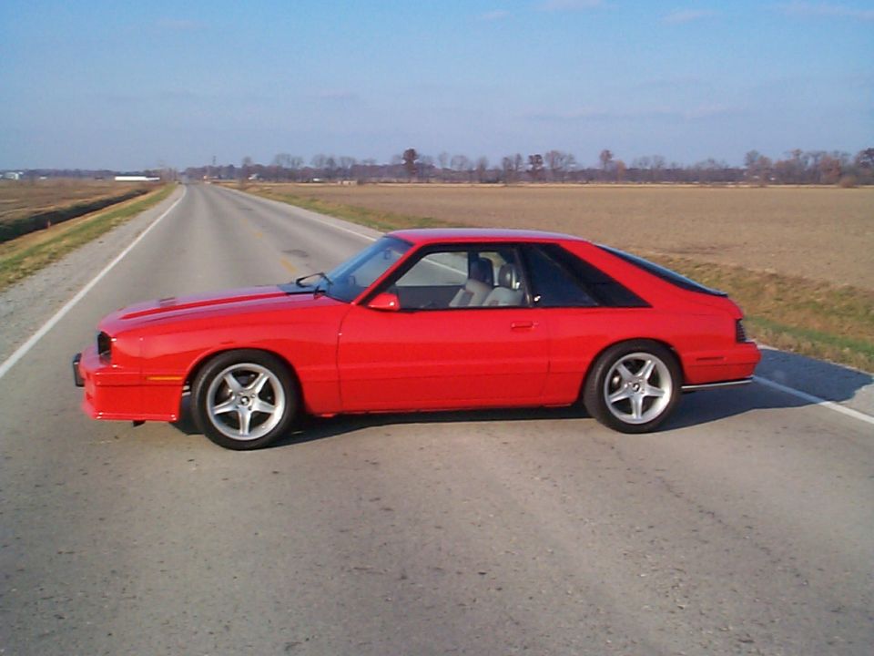 Red coupe with a fastback roofline parked on the side of a rural road