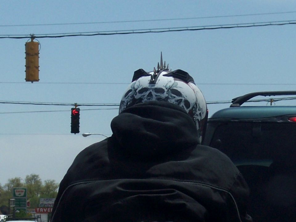 Motorcycle helmet with skull graphics and spikes, seen from behind, with a dark SUV to the right