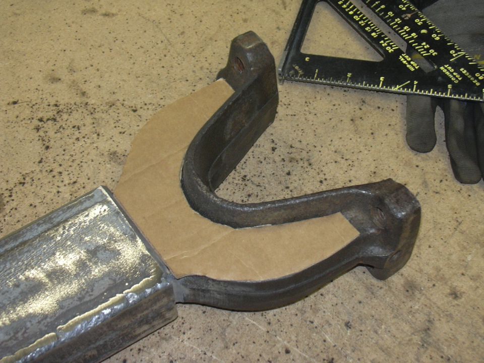 Metal part with a cardboard template on it, next to a speed square and gloved hand