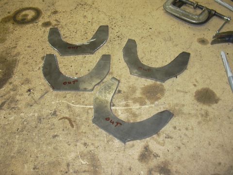 1991 Ford Bronco - Four metal brackets, possibly for a vehicle suspension, are laid out on a workbench. The word 'OUT' is written on each.