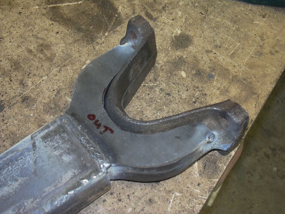 Metal suspension part with 'OUT' written in red marker, on a workbench