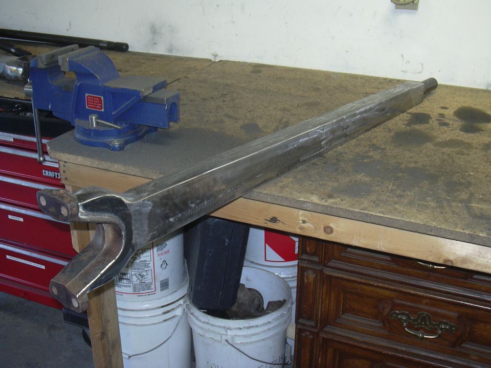 Metal suspension component with a Y-shaped bracket on a workbench next to a blue vise