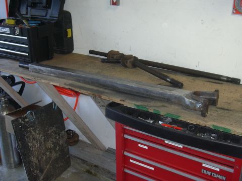 1991 Ford Bronco - These automotive parts, likely radius arms and drive shafts, are laid out on a wooden workbench next to a toolbox.