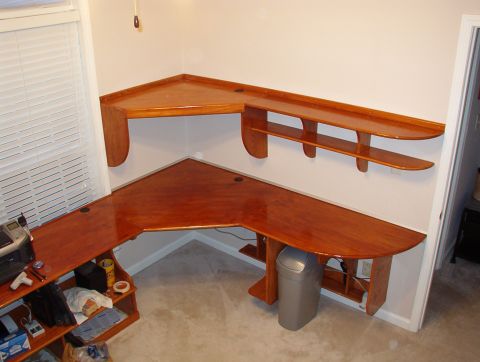 2004 Land Rover Land Rover - A wooden corner desk and shelving unit are shown in a room. A trash can is visible under the desk.