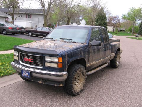 1995 GMC Sierra 1500 - A muddy 1995 GMC Sierra 1500 pickup truck is parked on a residential street.