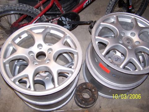1993 Ford Probe - Several alloy wheels are stacked, with a bicycle visible behind them. The image also contains a date stamp and a website logo.