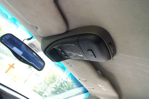 1999 Ford Crown Victoria - Interior overhead console of a car photographed sideways, showing a black overhead unit with reading lights, control buttons, and a mesh sp…