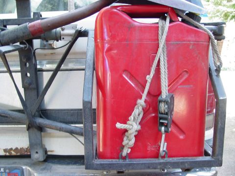 1986 Ford Bronco - A red jerry can is strapped to a vehicle's exterior rack with rope and a pulley system.
