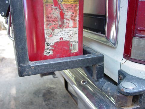 1986 Ford Bronco - A red jerry can is mounted on the rear bumper of a vehicle, with visible warning labels.