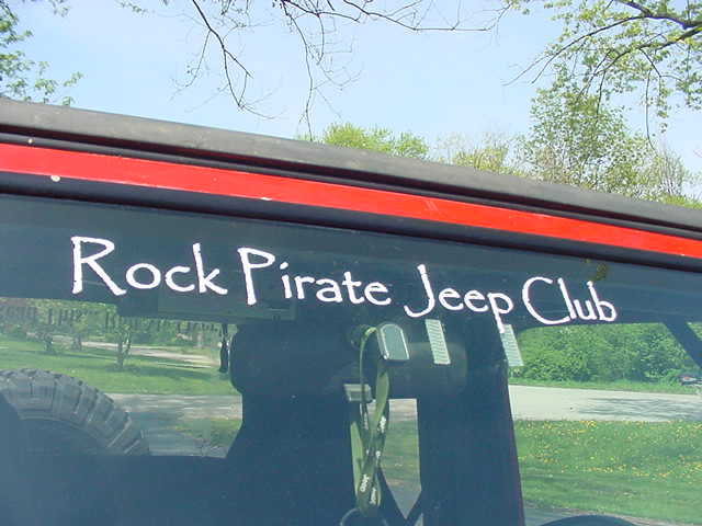 Side window of a Jeep with 'Rock Pirate Jeep Club' sticker. Spare tire visible