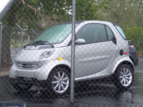 1972 Ford Ranchero - A silver Smart Fortwo is parked behind a chain-link fence on a cloudy day.