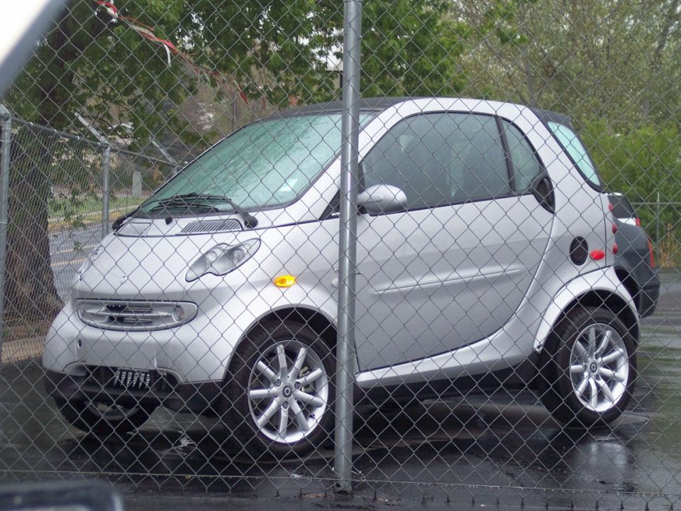 Silver Smart Fortwo behind a chain-link fence