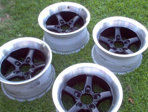1986 Ford Bronco - Four aftermarket five-spoke wheels with polished lips and black centers are displayed on a grassy surface.
