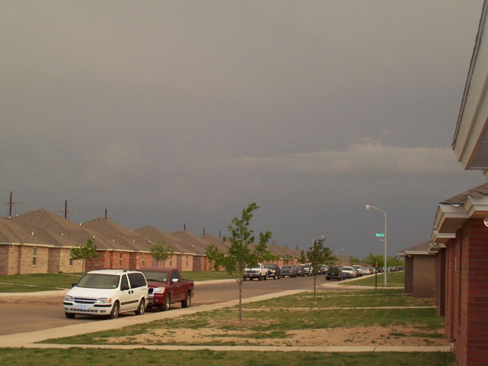 Street with parked cars and houses under a cloudy sky