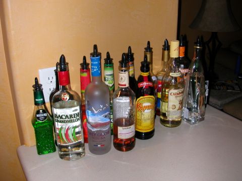 1984 Ford Bronco - A collection of various liquor bottles are lined up on a countertop next to a wall outlet.