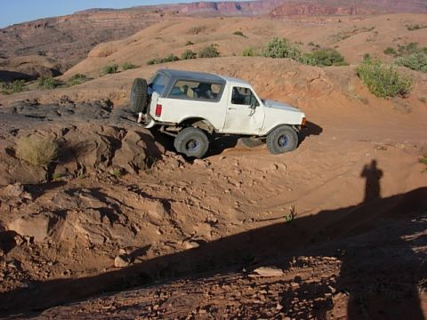 1987 Ford Bronco - A white SUV navigates a challenging off-road path in a desert landscape.