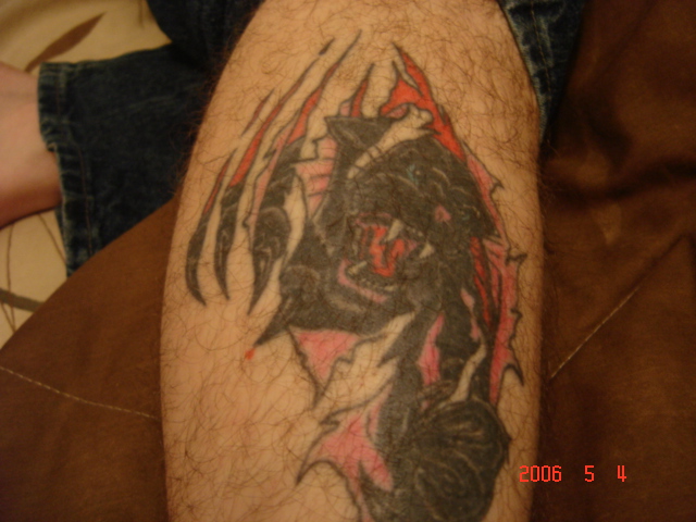 Tattoo of a black creature with red accents on a hairy leg