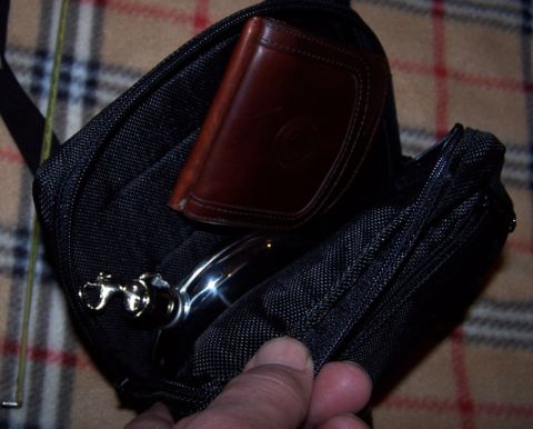 1990 Ford Bronco - A black bag contains a brown wallet and a metallic item, resting on a plaid surface.