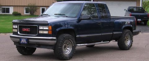 1995 GMC Sierra 1500 - A dark blue 1995 GMC Sierra 1500 pickup truck is parked in a driveway with another truck in the background.