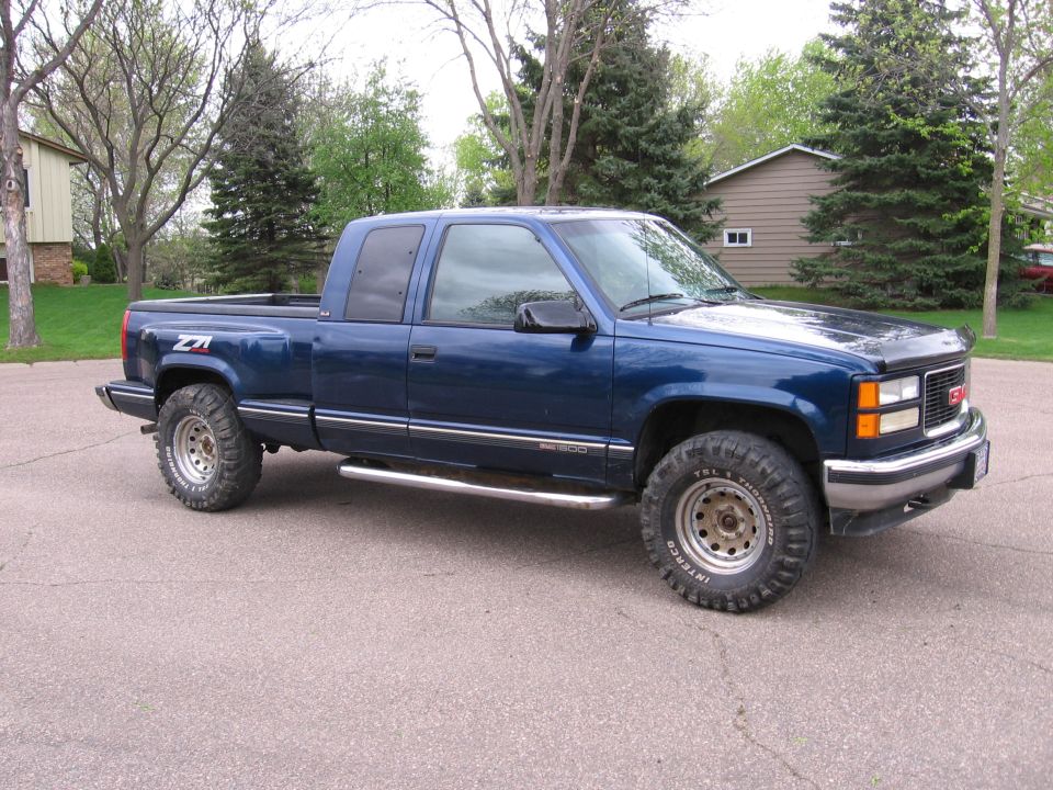 Dark blue GMC Sierra 1500 extended-cab pickup, front-right 3/4 view, lifted with mud tires.