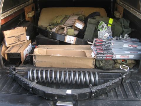 1979 Ford Bronco - The bed of a truck is filled with various items, including suspension components and boxes.