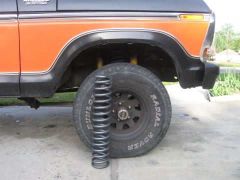 1979 Ford Bronco - A suspension coil is placed next to the front tire of an orange and black Ford Bronco.