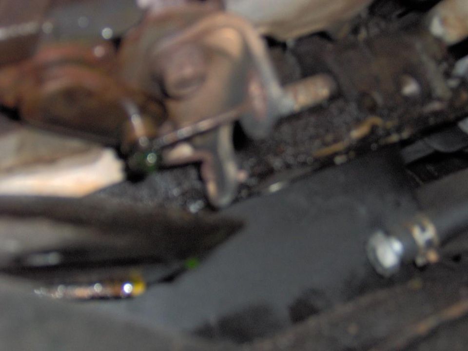 Blurry underbody view of greasy metal brackets and hoses beneath a vehicle